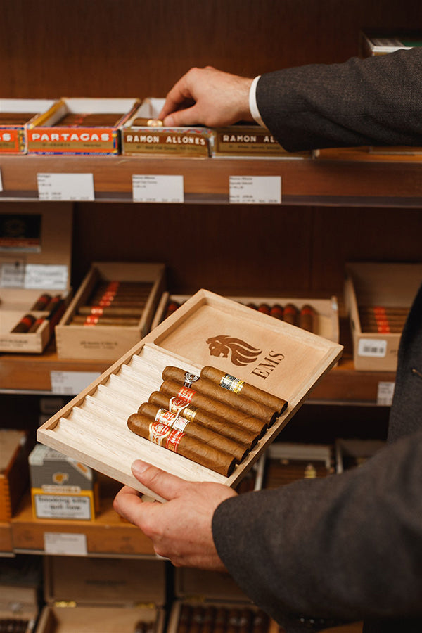 Person holding a box of cigars in a store with various cigar boxes on shelves.