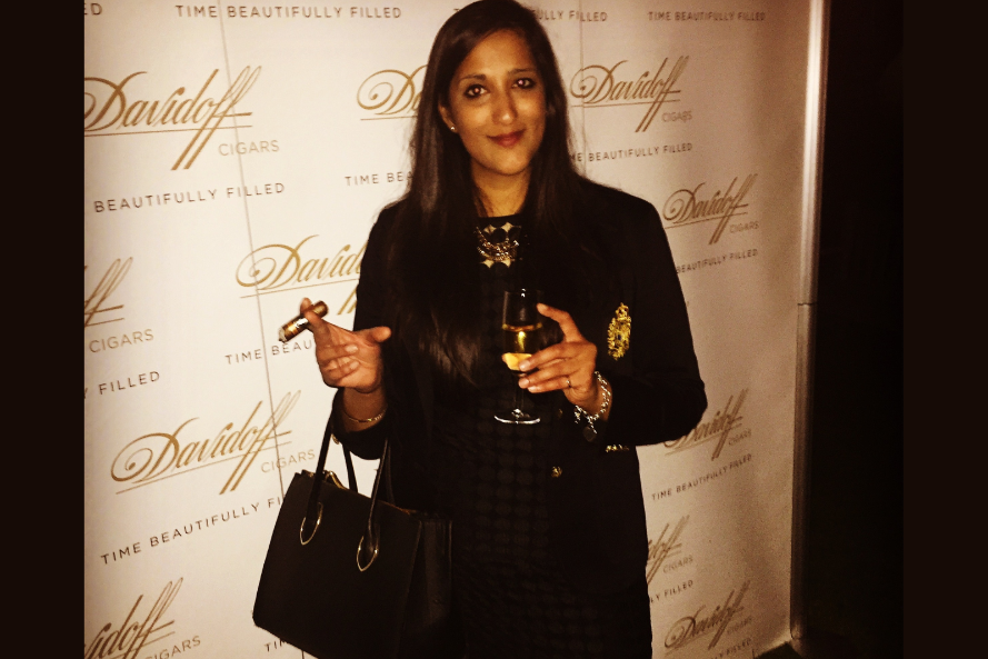 Woman holding a glass of wine and a cigar in front of a Davidoff branded backdrop